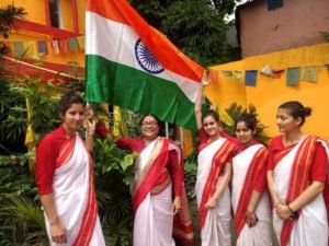 five women wearing sarees with a flag